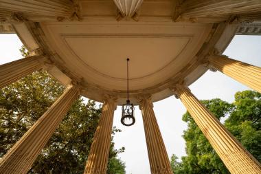 An upward view of a classical-style domed ceiling with an iron lantern hanging from the center, surrounded by corinthian columns.