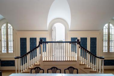 Double staircase with a white banister, behind it are full springline windows and blue panelling on the wall. 
