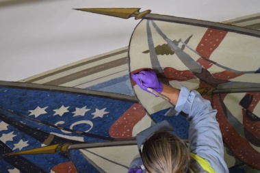 A conservator carefully touches up the canvas mural.