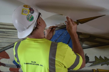 A conservator applies new adhesive where the canvas mural has started pulling away from the dome wall.