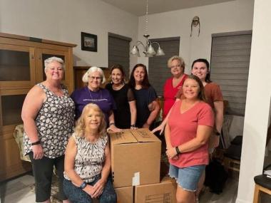 A group of members pose in front of boxes that they packed. 