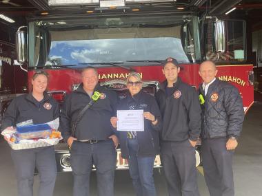 A member poses with fire men in front of a fire truck. 