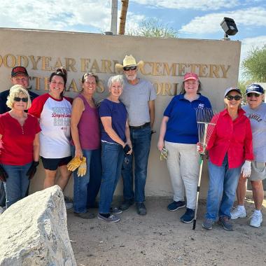 A group of members smiling in front of a cemetery entrance. 