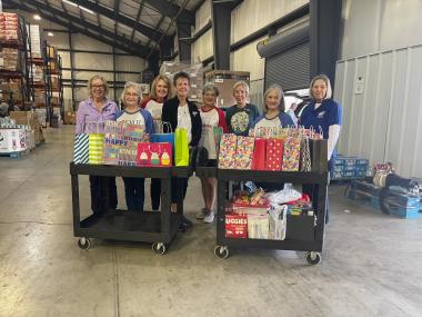 A group of DAR members stand in a warehouse with bags on a dolly.  