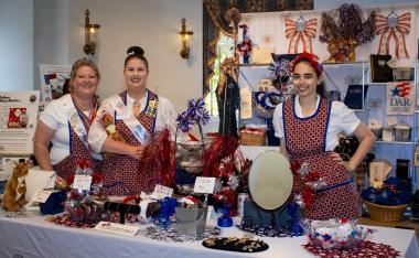 Women in red white and blue aprons sell patriotic items.