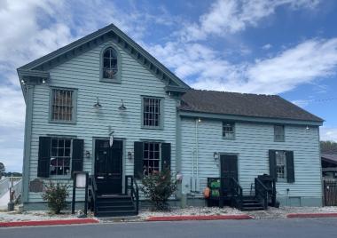 Teal blue house with dark blue shutters in front of a bright blue sky with clouds. 