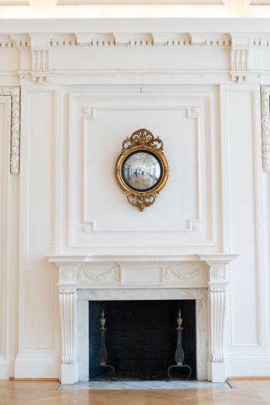 A decorative mantle with a fire place and a gold circular mirror above. 