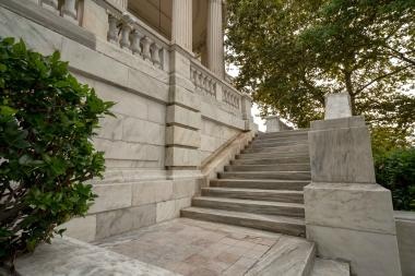  Stone steps with handrails leading to the entrance of a building, flanked by greenery.