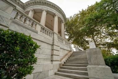 A set of stairs framed by lush greenery, leading up to the front entrance of a beautiful building.
