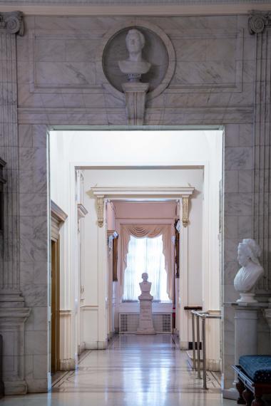 A hallway with a window at the end of it and a marble bust.