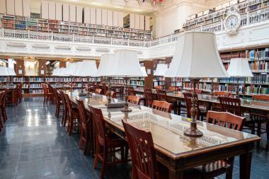 Library with rows of books and long tables with lamps on them