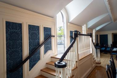 Looking up the double staircase which is surrounded by blue panelling and a full springline window that meets in the middle of the staircase. 